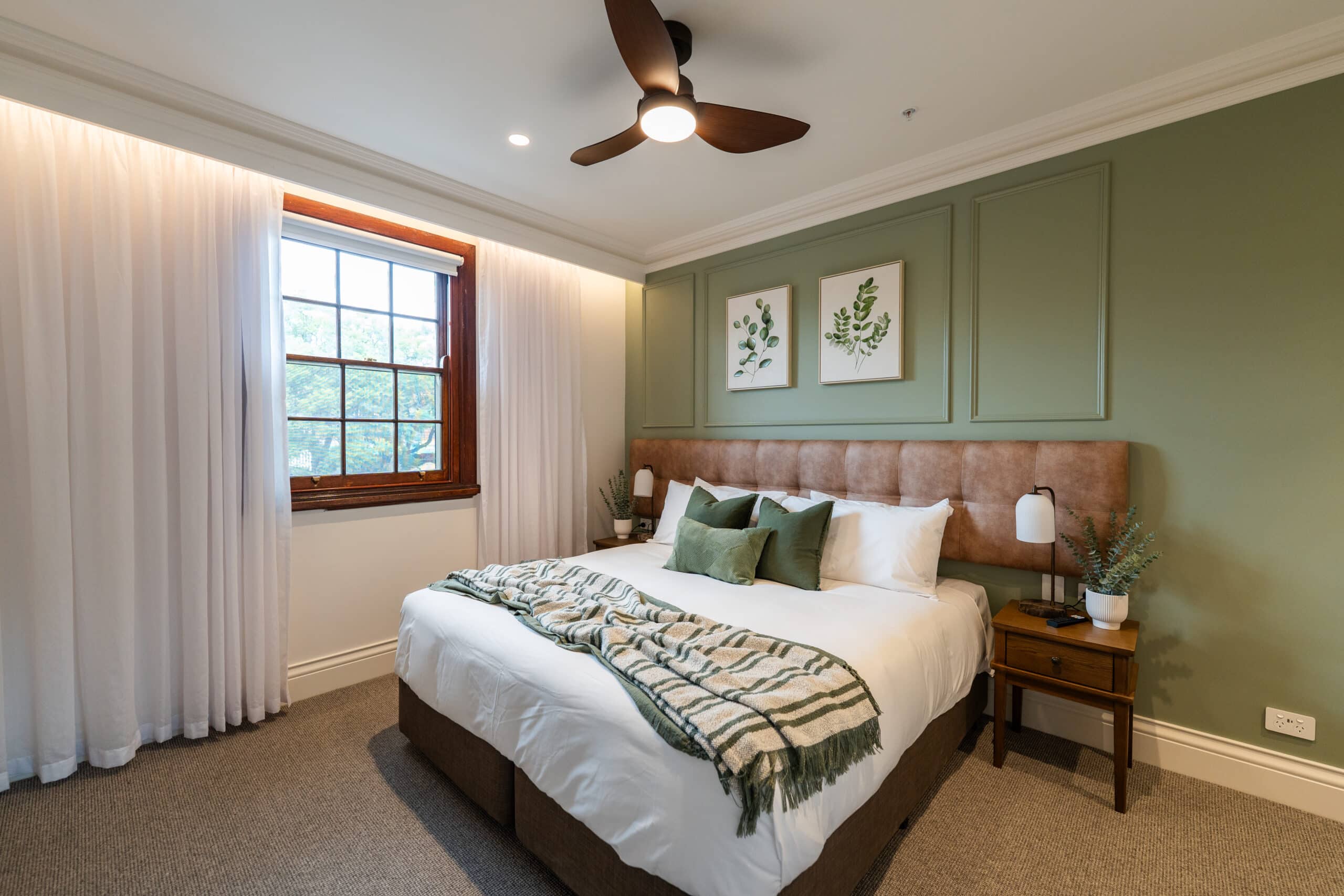 Guest room view showing sheer curtains and roller blind beside the bed.