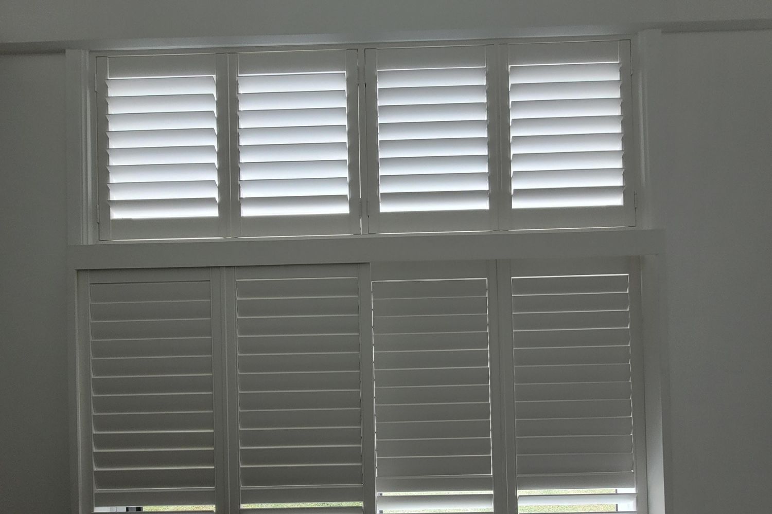 White PVC shutters installed on a tall interior window by Apollo Blinds Wollongong.
