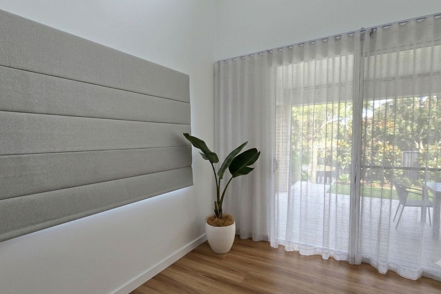 Soft grey Roman blind paired with sheer curtains in a Wollongong home, creating layered light control beside a glass door.