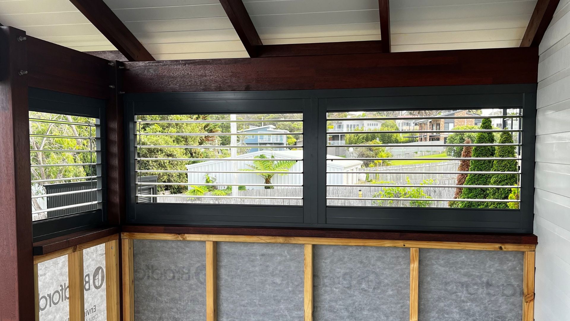 Black aluminium louvre shutters enclosing a covered patio dining area.