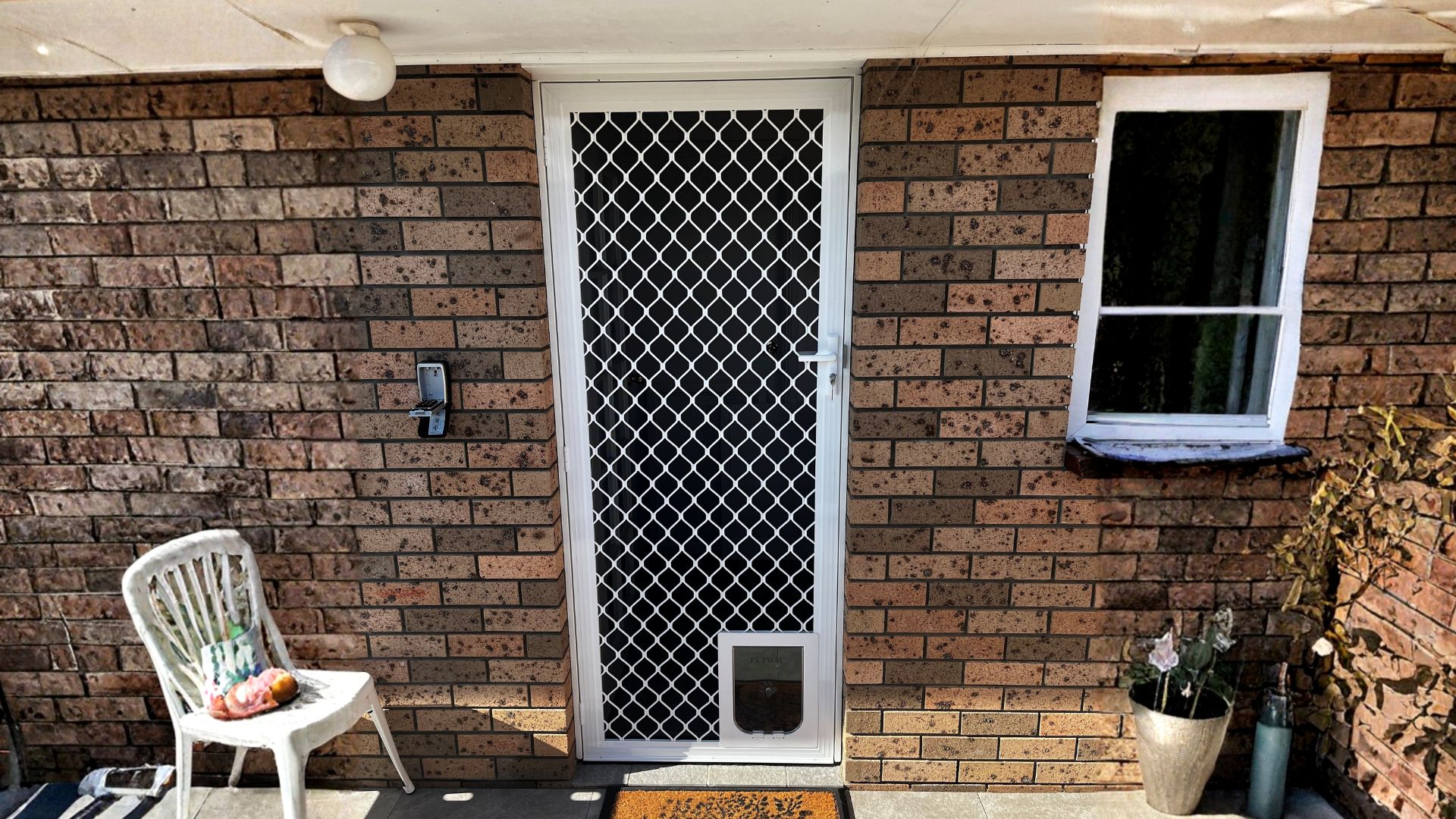 White hinged screen door with diamond grille and pet door installed on a brick South Coast home
