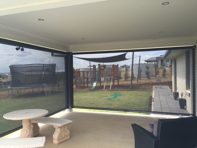 Black mesh Ziptrak outdoor blinds enclosing two sides of a covered patio in Greater New England by Apollo Blinds